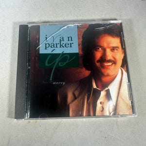 May include: A CD case featuring a smiling man with dark hair and a mustache. The CD cover has the text "Ivan Parker" and "up" in a stylized font, with the word "mercy" below. The case is clear plastic.