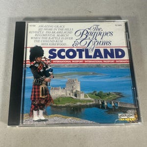 May include: A CD case with the title "The Bagpipes & Drums of Scotland." The cover shows a bagpiper in traditional Scottish dress, a castle, and the word "Scotland." The CD is in a clear plastic case.