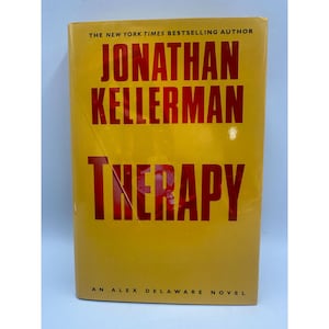 May include: A hardcover book titled "THERAPY" by Jonathan Kellerman. The book has a yellow cover with red lettering. The text "THE NEW YORK TIMES BESTSELLING AUTHOR" is at the top. The book is an Alex Delaware novel.