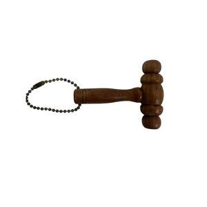 May include: A small, wooden gavel with a dark brown finish. The gavel has a rounded head and a handle. A metal ball chain is attached to the handle. The gavel is likely a miniature decorative item or a keychain.