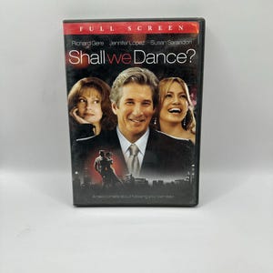 Puede incluir: Caja de DVD de la película "Shall We Dance?" con Richard Gere, Jennifer Lopez y Susan Sarandon. La portada tiene una pancarta roja en la parte superior con las palabras "FULL SCREEN". El título está en letras grandes y estilizadas.