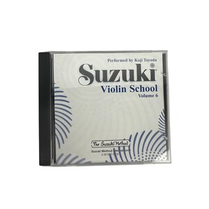Op de afbeelding: Een cd-hoesje met de tekst "Suzuki Violin School Volume 6" en de naam van de uitvoerder, Koji Toyoda. De hoes heeft een transparante voorkant en een zwarte rug. Het Suzuki Method-logo is ook zichtbaar.