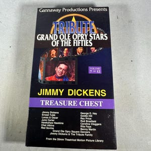 Pode incluir: Uma fita VHS preta com o título "Tribute Grand Ole Opry Stars of the Fifties". A fita apresenta uma foto de Jimmy Dickens e o texto "Treasure Chest". O volume 7 de 12 é exibido. A fita também lista os artistas.