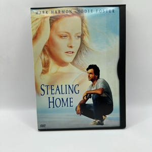 Puede incluir: Caja de DVD de la película "Stealing Home" con Mark Harmon y Jodie Foster. La portada muestra a una mujer rubia y a un hombre con camisa gris y vaqueros. El título está en letras azules grandes.