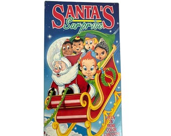 Pode incluir: Uma fita VHS intitulada "Santa's Surprise" com uma imagem de desenho animado do Papai Noel em um trenó vermelho com crianças. A capa tem um fundo azul com uma lua cheia e estrelas. O texto "PLUS 8 MORE COLOR CARTOONS" também é visível.