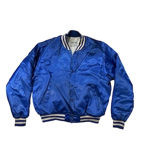 May include: A royal blue satin bomber jacket with a button-up front, white and blue striped cuffs and hem, and a white collar with blue trim. The jacket has a shiny, smooth texture and a classic, vintage style.