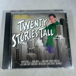 May include: A CD case featuring the album "Twenty Stories Tall" by Mark Lowry. The cover art includes a cityscape, the artist in a green jacket, and the album title in large white letters. The CD case is clear.
