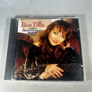 Puede incluir: Una caja de CD con el álbum de Pam Tillis, "Sweetheart's Dance". La portada muestra a una mujer con cabello castaño rojizo, vestida con un top de terciopelo oscuro y apoyando sus manos con un anillo en el dedo. El título del álbum está en una fuente decorativa.