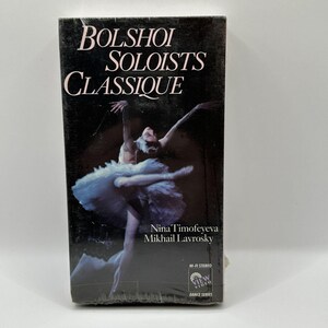 Pode incluir: Uma fita VHS com o título "Bolshoi Soloists Classique" em texto branco sobre fundo preto. A capa apresenta uma bailarina com um tutu branco. Os nomes Nina Timofeyeva e Mikhail Lavrosky também são visíveis.