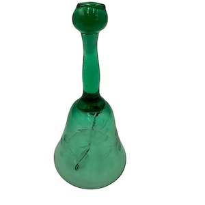 Puede incluir: Una campana de vidrio verde con un tallo largo y una parte superior redonda. La campana tiene una base acampanada y diseños florales grabados. La campana está hecha de vidrio verde transparente.
