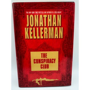 May include: A red hardback book by Jonathan Kellerman, titled "The Conspiracy Club". The cover features gold lettering and decorative patterns. The author's name is at the top, with the title in a gold box.