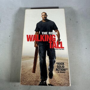 May include: A DVD case for the movie "Walking Tall" featuring Dwayne "The Rock" Johnson. The cover art shows Johnson walking towards the viewer, holding a wooden object. The title is in large red letters.