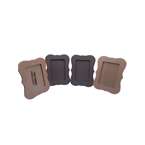 May include: Four decorative picture frames in shades of brown and grey. Each frame has a unique, ornate shape with a rectangular opening. One frame contains a small object. The frames are arranged in a row against a white background.