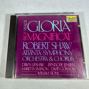 May include: A CD case featuring the album "Gloria/Magnificat" by Bach Vivaldi, performed by the Atlanta Symphony Orchestra & Chorus, with Robert Shaw. The cover is a deep purple with teal and pink text. The CD case is in a clear plastic case.