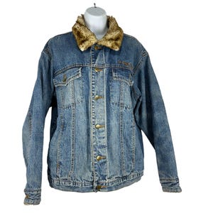 May include: A blue denim jacket with a faux fur collar. The jacket has a button-up front, two chest pockets, and two side pockets. The collar is a mix of brown and tan colors. The jacket is displayed on a white mannequin.