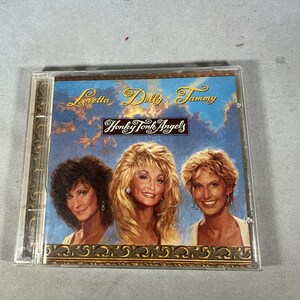 May include: A CD case featuring the album "Honky Tonk Angels" with portraits of Loretta, Dolly, and Tammy. The album cover has a blue sky background with gold lettering and a decorative border.