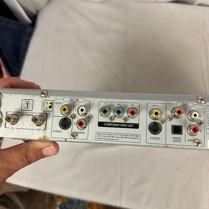Pode incluir: Dispositivo eletr&ocirc;nico prateado com m&uacute;ltiplas portas de entrada e sa&iacute;da. Possui conex&otilde;es de antena, v&iacute;deo, &aacute;udio e sa&iacute;da de v&iacute;deo componente. O dispositivo possui conectores coloridos para f&aacute;cil identifica&ccedil;&atilde;o.