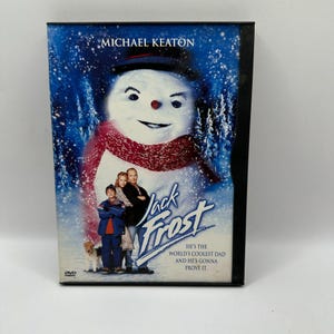 May include: A DVD case for the movie Jack Frost featuring Michael Keaton. The cover art displays a large snowman wearing a black hat and red scarf, with a family and a dog standing in front. The text reads Jack Frost, He's the world's coolest dad.