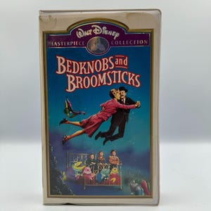 May include: A VHS tape of the Disney movie "Bedknobs and Broomsticks" from the Masterpiece Collection. The cover art features a couple dancing in the air, with children and animated creatures below. The title is in red and white lettering.