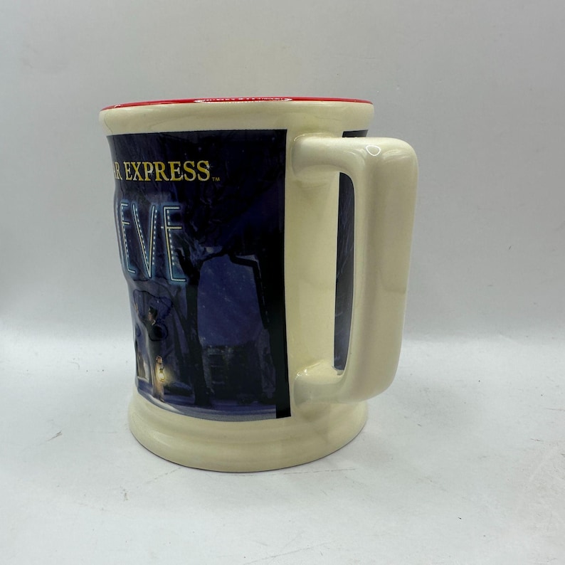 May include: Cream-colored ceramic mug with a rectangular shape and a large handle. The mug features a dark blue graphic with the words "POLAR EXPRESS" and "BELIEVE" in white lettering. The rim is red.