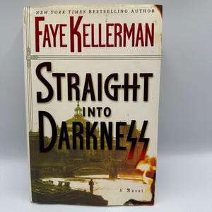 May include: A hardcover book titled "Straight Into Darkness" by Faye Kellerman. The cover features a cityscape with a bridge and a fiery explosion. The author's name is in red, and the title is in black.