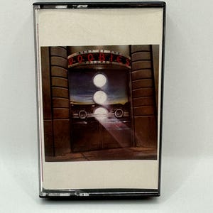 May include: A vintage cassette tape featuring the album "Best of the Doobies Volume 2." The cassette case is black, and the album art shows a stylized image of a doorway with the band's name in red lettering.