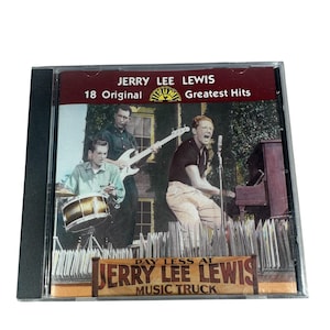 May include: A CD case featuring Jerry Lee Lewis's "18 Original Greatest Hits." The cover art shows Lewis performing with a band. The text "Pay Less at Jerry Lee Lewis Music Truck" is also visible.