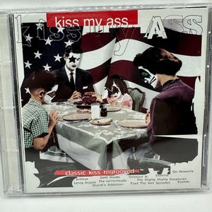 May include: CD case with the album cover for "Kiss My Ass." The cover features a family at a table with painted faces, in front of an American flag. The text "classic kiss regrooved" is at the bottom.