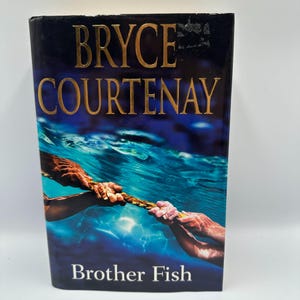 May include: A hardcover book titled "Brother Fish" by Bryce Courtenay. The cover features a blue underwater scene with hands holding a rope. The author's name is in gold lettering.