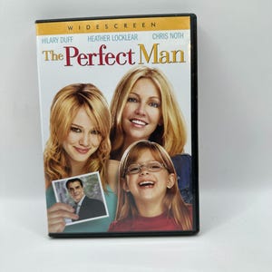 Puede incluir: Una carátula de DVD de la película "The Perfect Man" con Hilary Duff, Heather Locklear y Chris Noth. La portada muestra a tres mujeres y una foto de un hombre. El título está en letras rojas grandes.