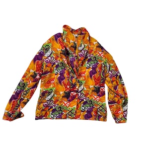 May include: A long-sleeved blouse with a vibrant floral pattern in shades of orange, purple, green, and red. The blouse features a collared neckline and button details. The fabric has a silky appearance.