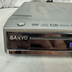 Pode incluir: Leitor de DVD Sanyo prateado com bot&atilde;o de ligar/desligar e nome da marca. Apresenta logotipos de DVD, Compact Disc Digital Audio e Dolby Digital. Inclui um n&uacute;mero de atendimento ao cliente.