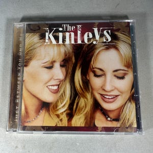 May include: CD case featuring two women with blonde hair. The text "The Kinleys" is at the top, with the album title "Just Between You And Me" on the side. The women are smiling, and wearing necklaces.