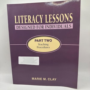 Puede incluir: Un libro titulado "Literacy Lessons Designed for Individuals" con "Part Two Teaching Procedures" en un óvalo en la portada. La portada es de color púrpura oscuro con texto dorado y blanco. El nombre del autor, Marie M. Clay, está en la parte inferior.