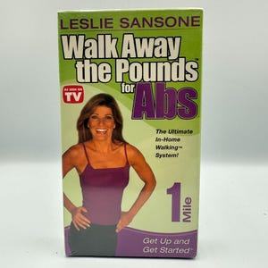 May include: A green and purple box for Leslie Sansone's "Walk Away the Pounds for Abs" fitness program. The box features a woman in workout attire and the text "As Seen on TV." It promotes an in-home walking system.