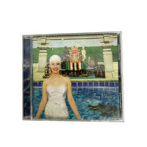 May include: A CD case featuring a woman in a white dress and swim cap in a pool with an alligator. The background includes a decorative structure and the text "Tiny Music..."