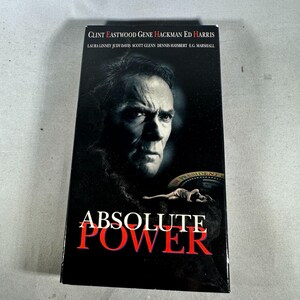 Può includere: Una videocassetta VHS nera del film "Absolute Power" con Clint Eastwood, Gene Hackman ed Ed Harris. La copertina presenta un ritratto di Clint Eastwood e il titolo in rosso.