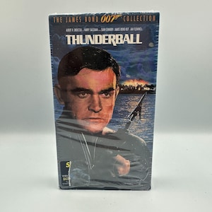 May include: A VHS tape of the James Bond film "Thunderball" from the 007 Collection. The cover features a portrait of Sean Connery and the film's title in bold white letters against a dark blue background. The tape is sealed in plastic.