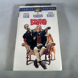 Puede incluir: Una cinta VHS de la película "Doctor Dolittle" con Rex Harrison, Samantha Eggar y Anthony Newley. La portada muestra a un hombre sentado con un mono y un perro.