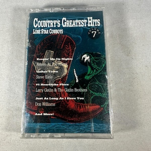Könnte beinhalten: Eine Musikkassette mit dem Album "Country's Greatest Hits: Lone Star Cowboys, Volume 7". Das Cover zeigt einen roten Cowboy-Stiefel, eine grüne Schlange und Songtitel. Die Kassette befindet sich in einer transparenten Kunststoffhülle.