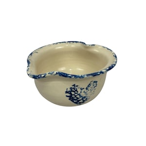 以下が含まれることがあります： 青い縁と側面の青い花の模様が特徴の、オフホワイトの小さなセラミックボウル。ボウルはわずかに不規則な形状で、注ぎ口が付いています。内側はクリーム色です。