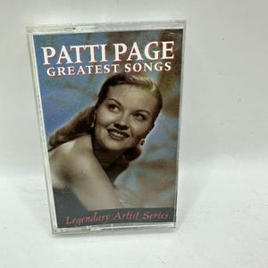 Può includere: Una musicassetta vintage con "Greatest Songs" di Patti Page. La copertina mostra un ritratto di Patti Page con il testo "Patti Page Greatest Songs" in lettere bianche e rosse. La parte inferiore della cassetta recita "Legendary Artist Series."