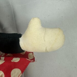 May include: Close-up of a vintage stuffed toy hand. The hand is made of off-white fabric with visible stitching. A black fabric section and a red fabric with white polka dots are also visible.