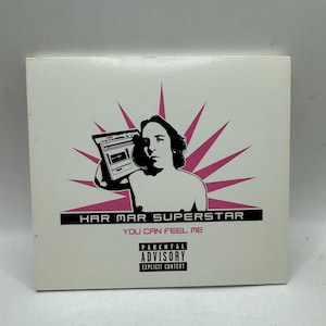 Op de afbeelding: Een witte vierkante cd-hoes met een zwart-roze afbeelding van een persoon die een boombox vasthoudt. De tekst luidt HAR MAR SUPERSTAR, YOU CAN FEEL ME, en bevat onderaan in het midden een zwart-wit Parental Advisory Explicit Content-label.