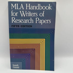 May include: A hardcover book titled "MLA Handbook for Writers of Research Papers, Fifth Edition." The cover is dark blue with white text and a colorful geometric design in shades of green, yellow, orange, and brown.