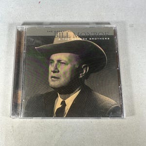 Può includere: Custodia per CD con un'immagine in bianco e nero di Bill Monroe con un cappello da cowboy. Il testo sulla copertina recita "THE ESSENTIAL BILL MONROE & THE MONROE BROTHERS."