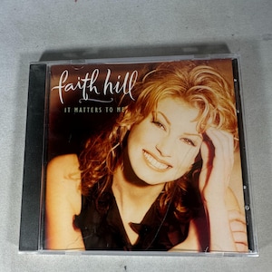 Puede incluir: Caja de CD con el álbum "It Matters to Me" de Faith Hill. La portada muestra a una mujer sonriente con cabello rubio. El título del álbum y el nombre del artista están en cursiva. La caja es transparente con un lomo negro.