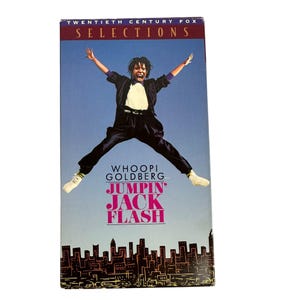 Pode incluir: Uma fita VHS do filme "Jumpin' Jack Flash" com Whoopi Goldberg. A capa apresenta uma pessoa saltando com os braços estendidos contra um fundo de céu azul. Uma vista da cidade na parte inferior.