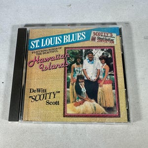 May include: A CD case for the album "St. Louis Blues Featuring Songs of the Beautiful Hawaiian Islands" by DeWitt "Scotty" Scott. The cover art shows a group of people in Hawaiian clothing. The CD case is in a clear plastic case.