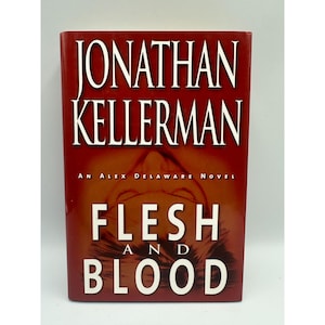 May include: A hardcover book titled "Flesh and Blood" by Jonathan Kellerman. The book has a red cover with white text. The author's name is at the top, and the title is in large letters. The book is part of the Alex Delaware novel series.